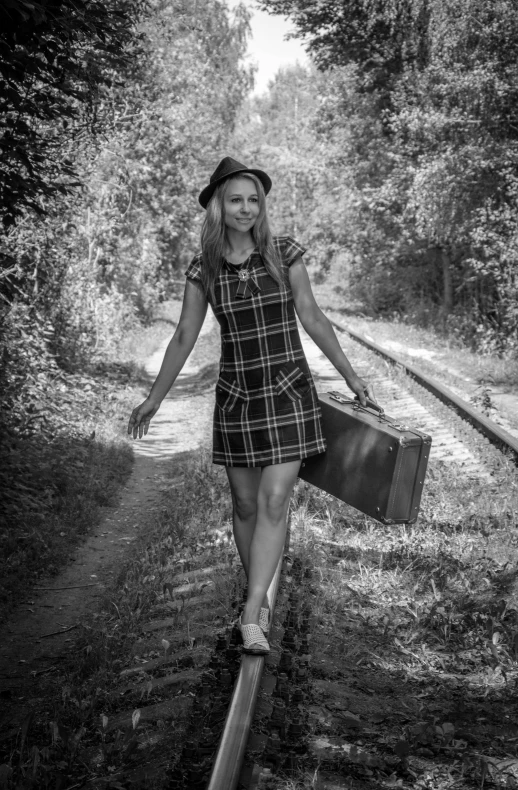 a woman carrying a suitcase walks along the tracks with a train