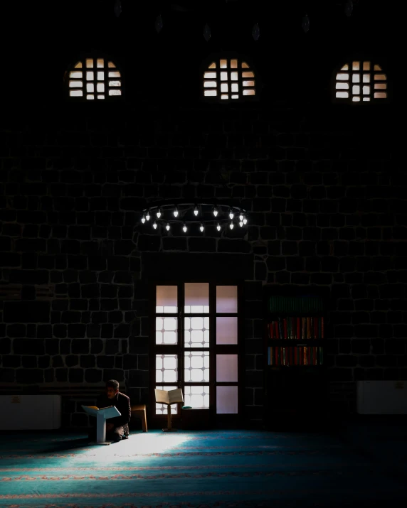 a dark, empty room has three windows and a person sitting down