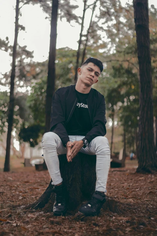 a young man in black jacket sitting on tree stump