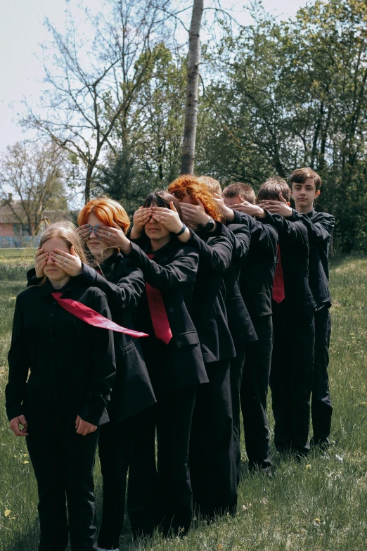 a group of women in ties are lined up with their hands covering their faces