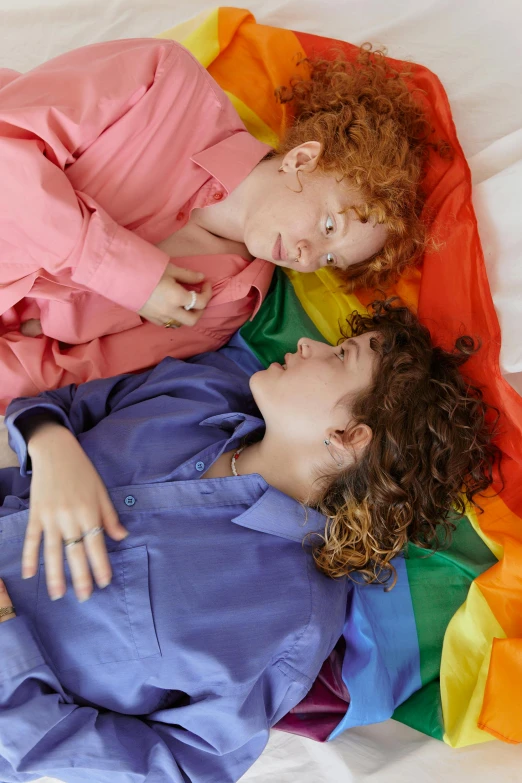 two woman laying on a white bed with a rainbow blanket