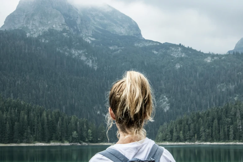 person looking at mountain range with trees reflected in water