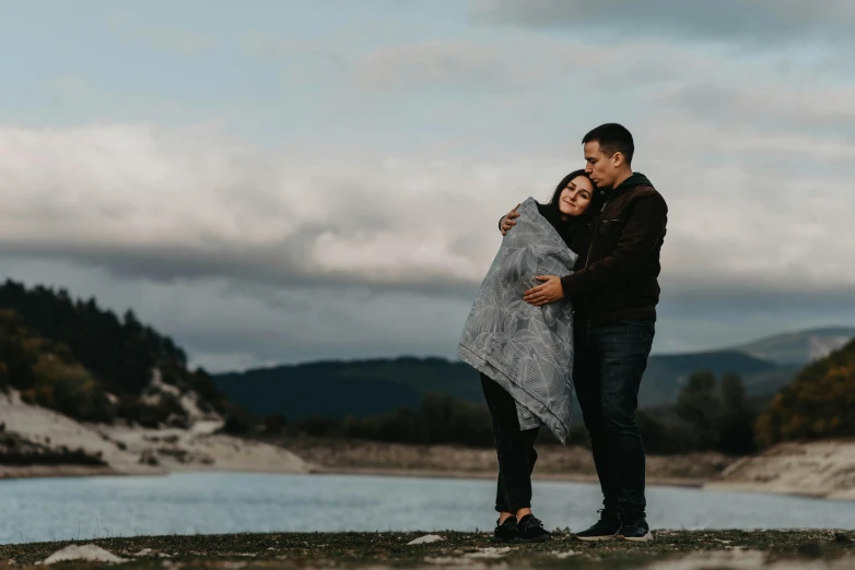 a man and woman hug each other while standing next to a mountain lake