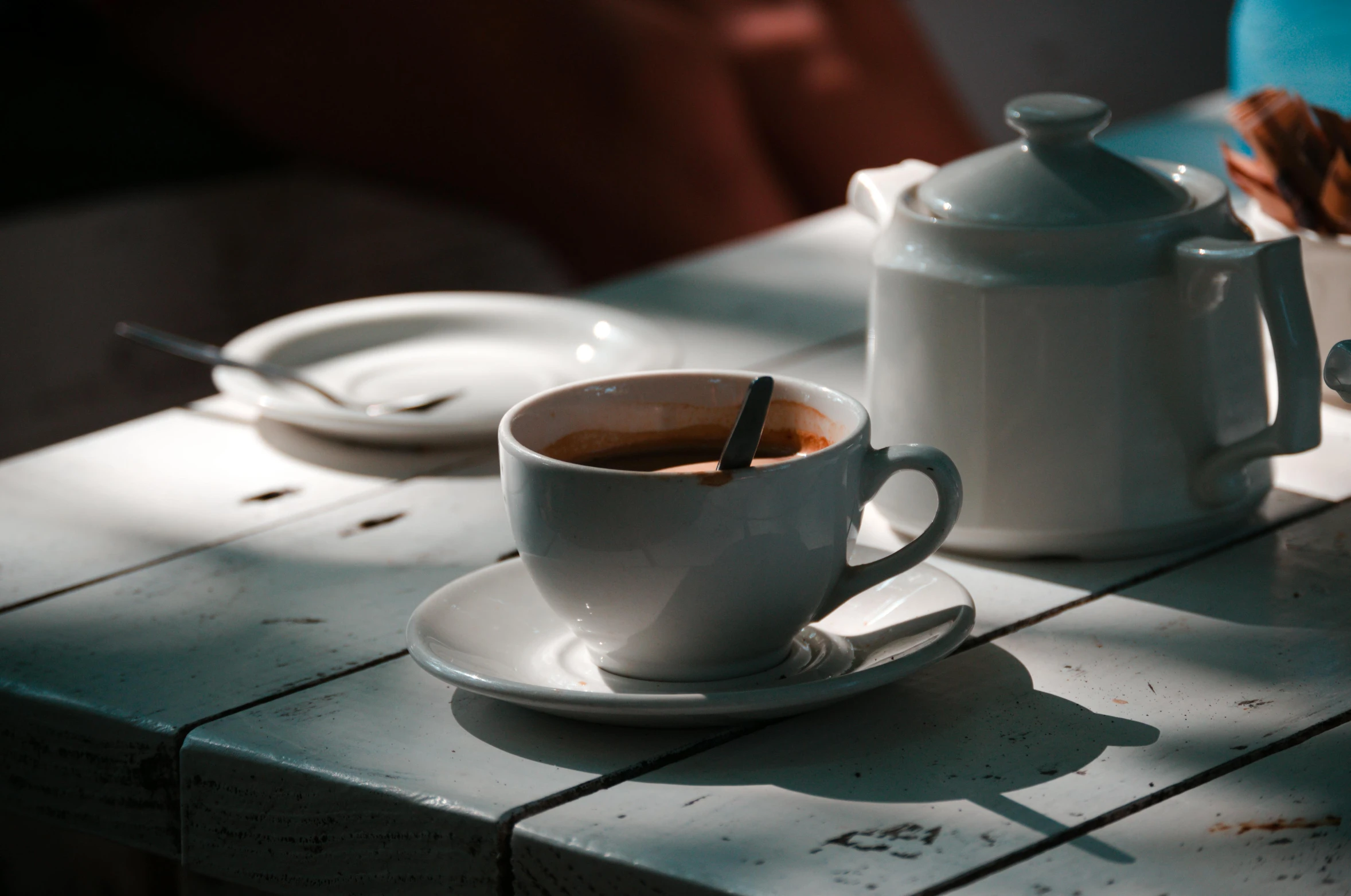 a white coffee pot and saucer with a spoon sitting on a table