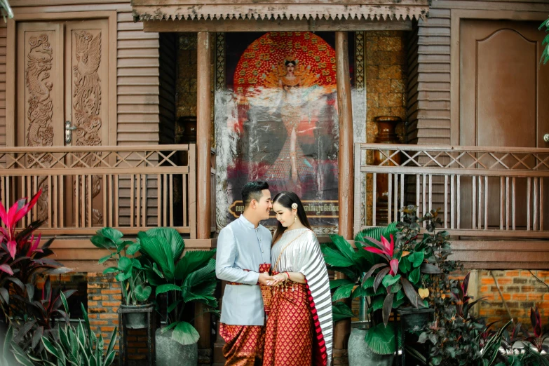 two asian people standing outside with flowers in front of a building