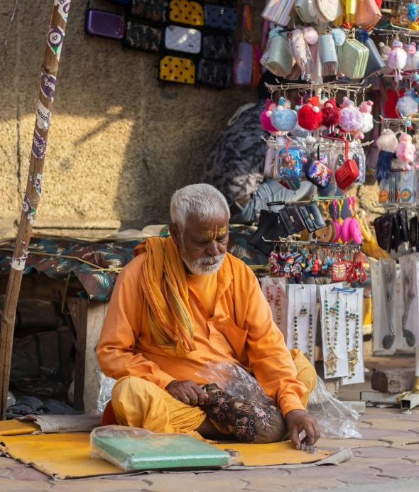 an old man sitting in front of a store selling items