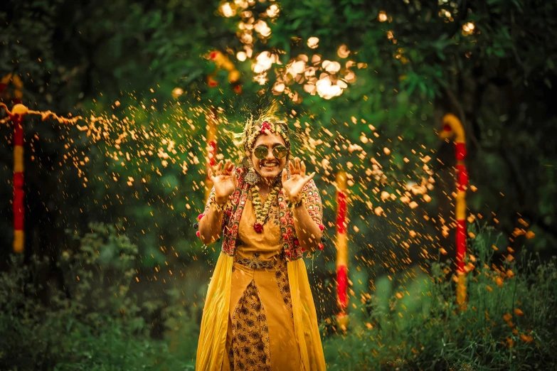 a woman dressed in a yellow and orange indian dress stands beneath rain falling from her hair