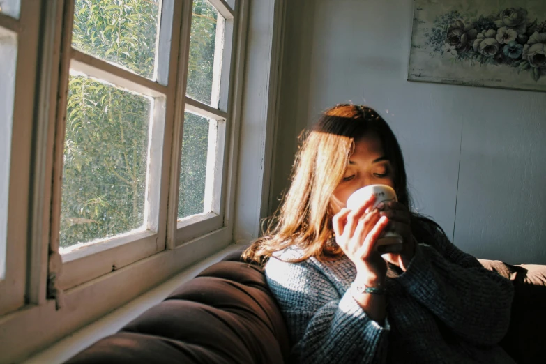 a person is sitting by a window taking a drink of soing