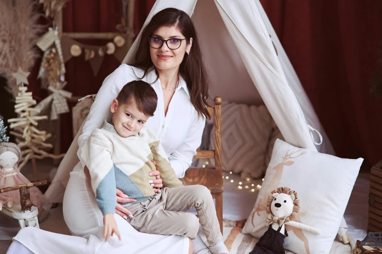 a woman holding her son while he sits in front of the bed