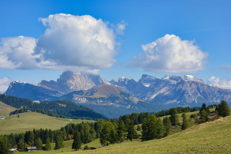 a green pasture and mountains under a cloudy blue sky