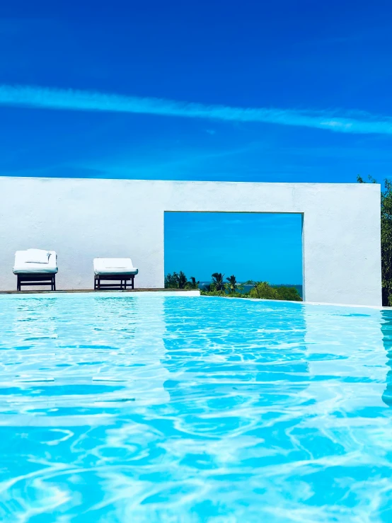 two chairs next to the swimming pool with clear blue water