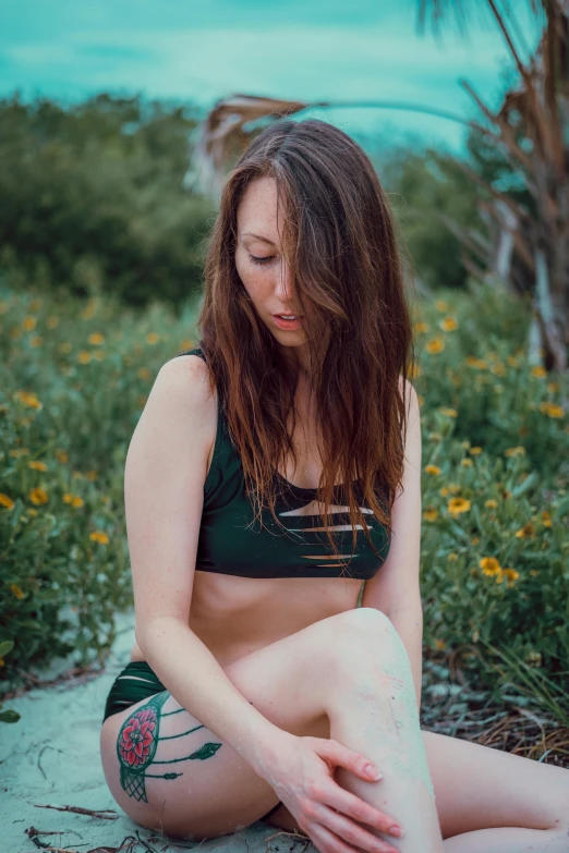 a woman wearing a bikini top sits on a beach