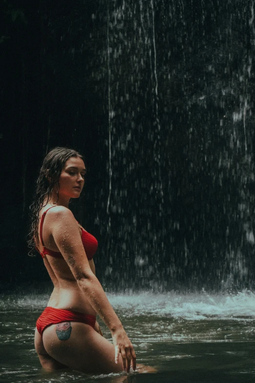 a lady in a red bikini in a body of water next to a waterfall