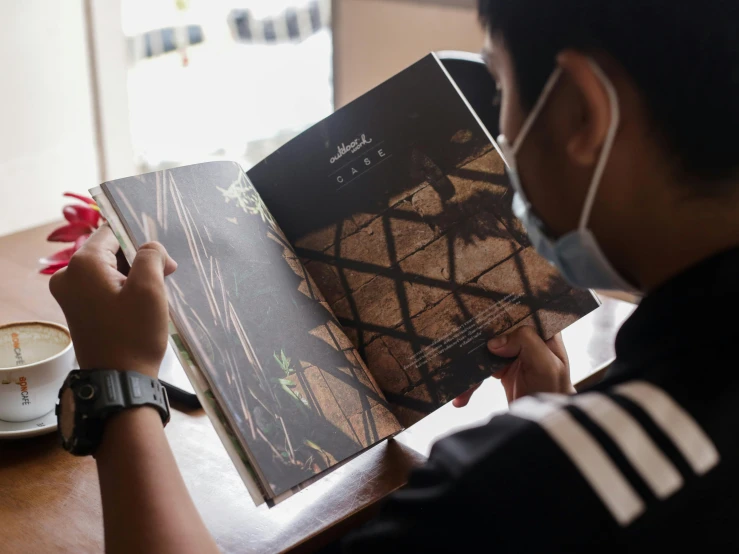 a boy wearing a face mask reading a book on the table