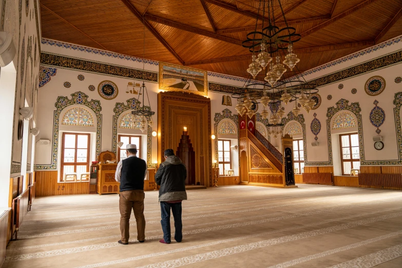 two people are standing in a large room with elaborate wall covering