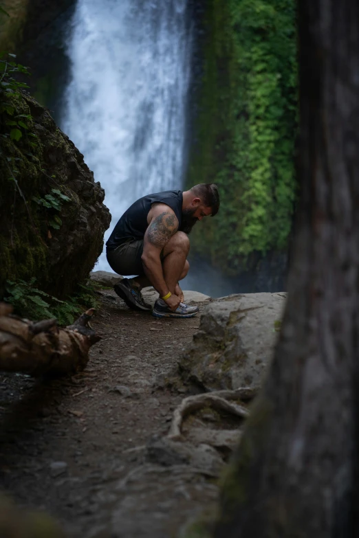 a man squatting on a rock next to a waterfall