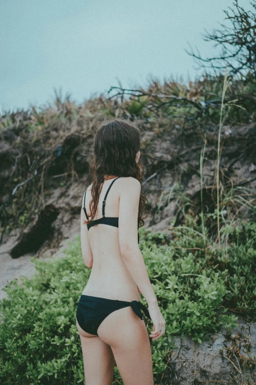 a woman with long hair and  stands near some bushes