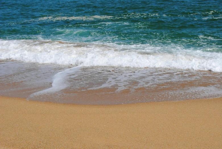 the small waves roll in on the beach sand