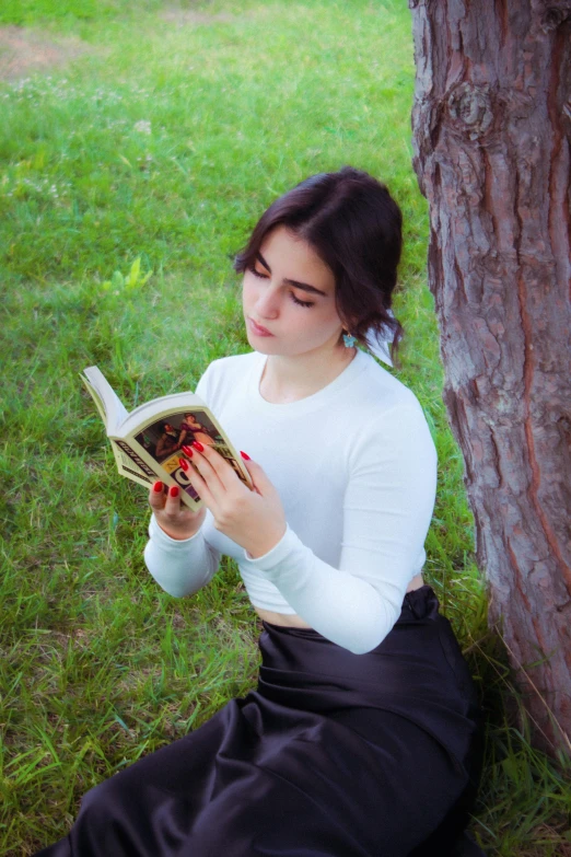 a girl is reading a book sitting by the tree