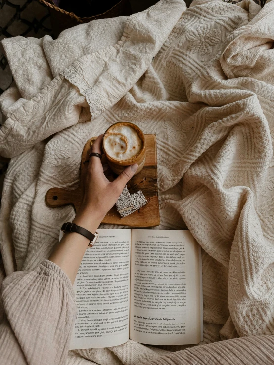 a person holding a book and a cup on top of an open book