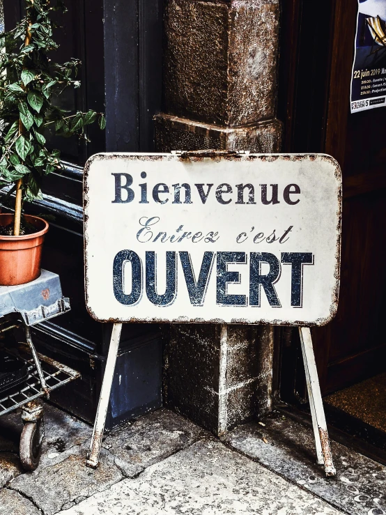 an old sign sitting on top of a street next to a plant