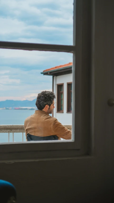 a man looking out of a window at the ocean