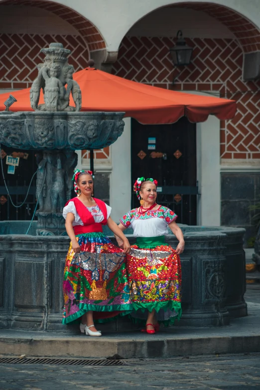 two women in folk costumes stand next to an ornate fountain