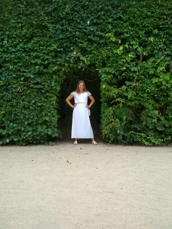 a woman standing in front of a very tall wall covered in bushes