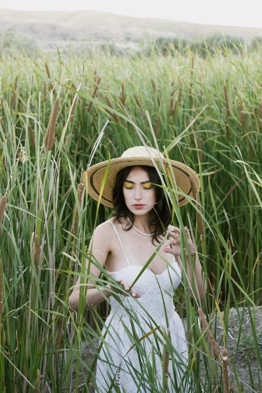 a woman in white dress and straw hat standing in a field of tall grass