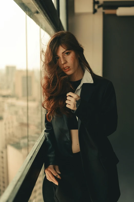 a woman with long red hair stands in an empty room with a city view