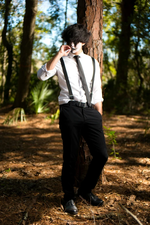 a boy wearing a suit and tie leaning against a tree