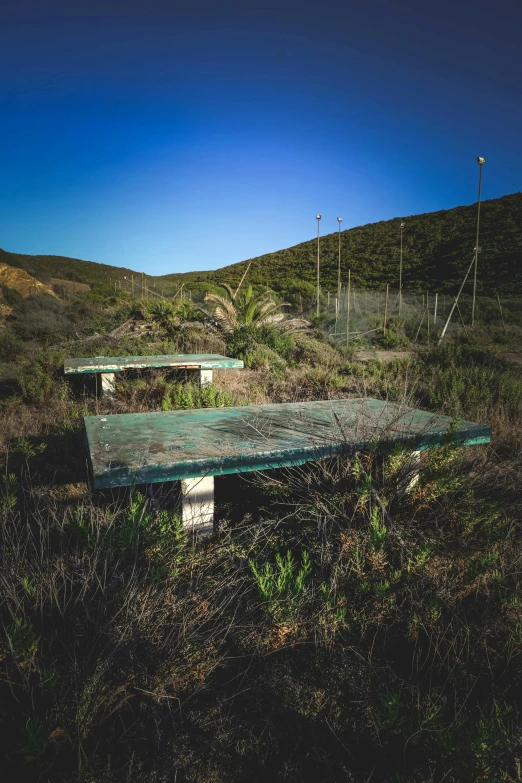 an empty bench near a field with hills in the background