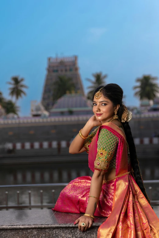 a woman wearing a pink and gold saree posing on a balcony