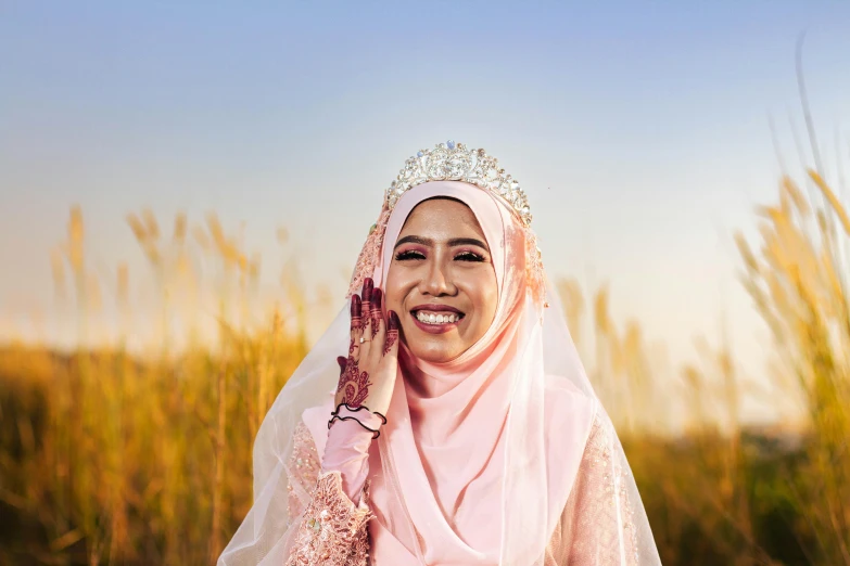 a young woman in a hijab poses for a po in front of tall grass