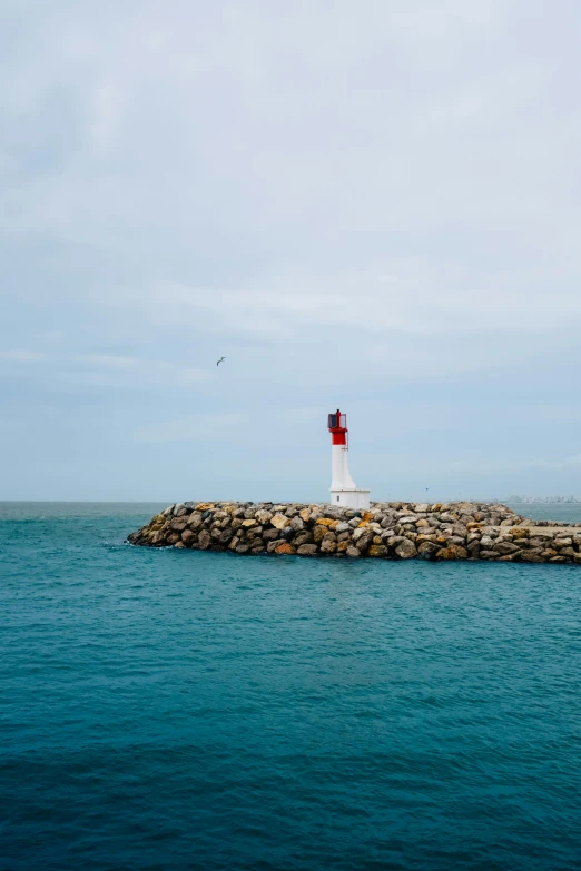 lighthouse sitting at the end of a pier with water in the foreground