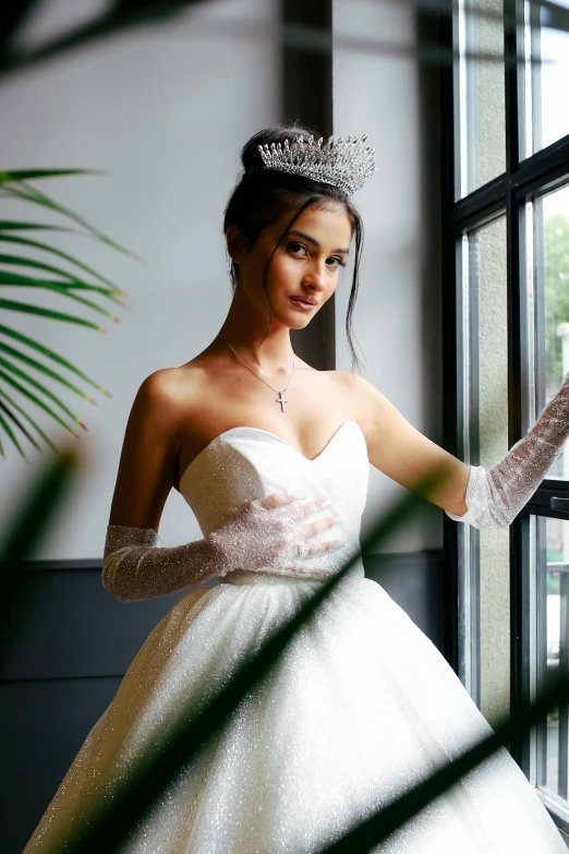 a beautiful young lady in a white dress standing near a window