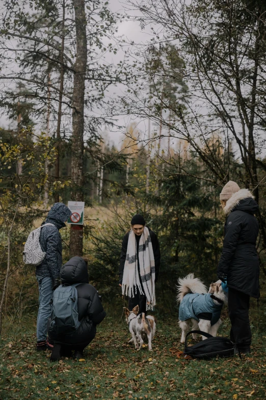 three adults and two dogs wearing coats standing on a field with a sign