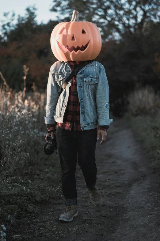 man in denim jacket wearing a jack o lantern mask on head