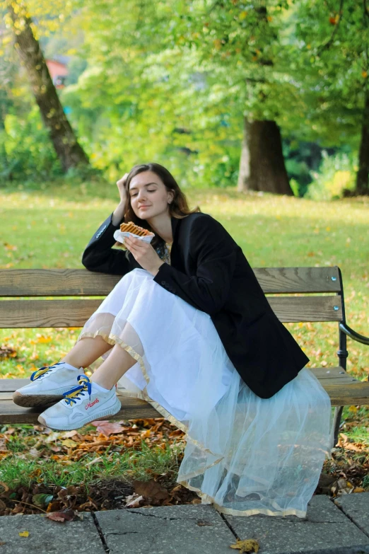 a woman is sitting on a bench in the park eating a sandwich