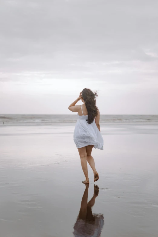 woman in white dress standing on the beach, looking into water