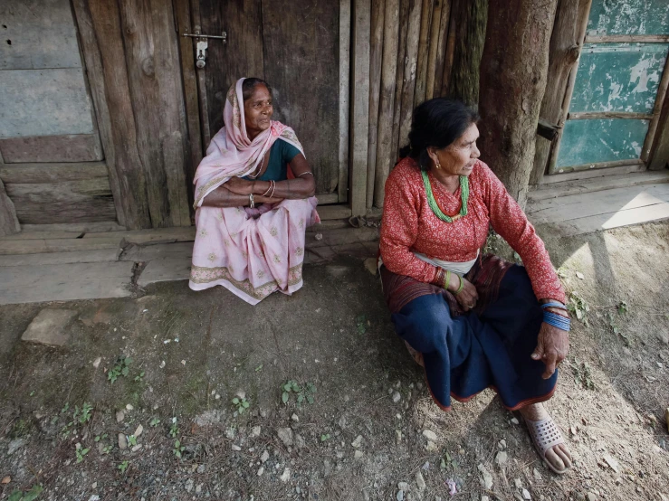 two women sit and talk in front of an old wooden structure