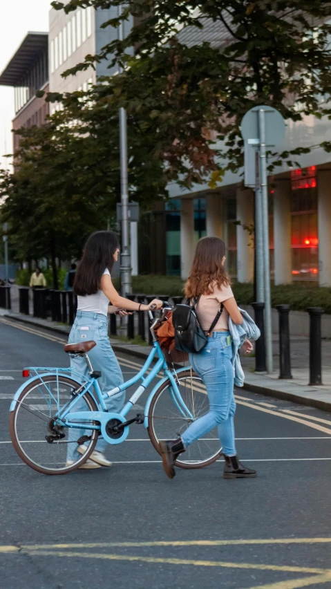 two girls are crossing the street with a blue bike