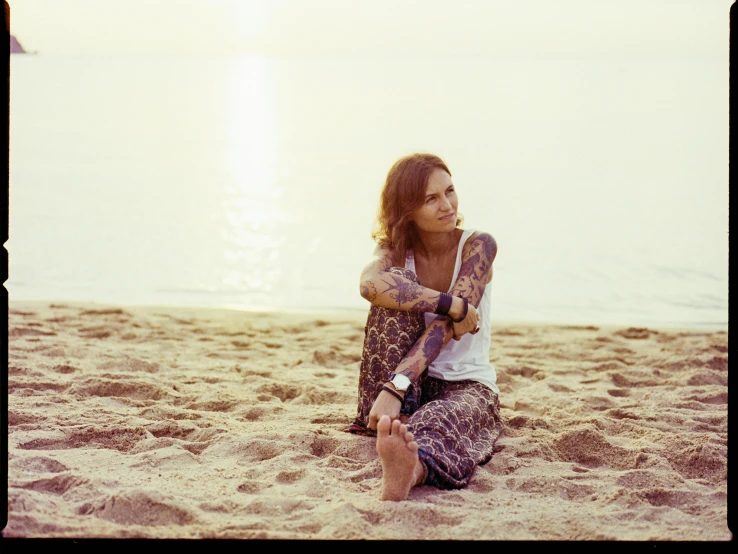 a young woman in her 30's sits on the beach holding up a board