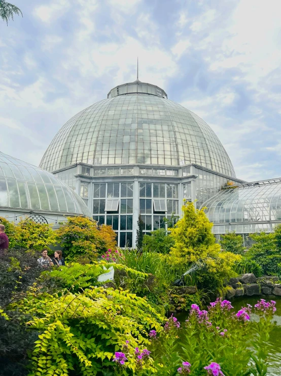 a clear glass greenhouse with green roof and trees