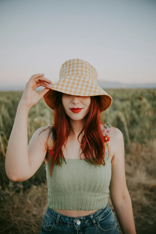 a young red - haired woman with red hair and plaid hat stands in a field