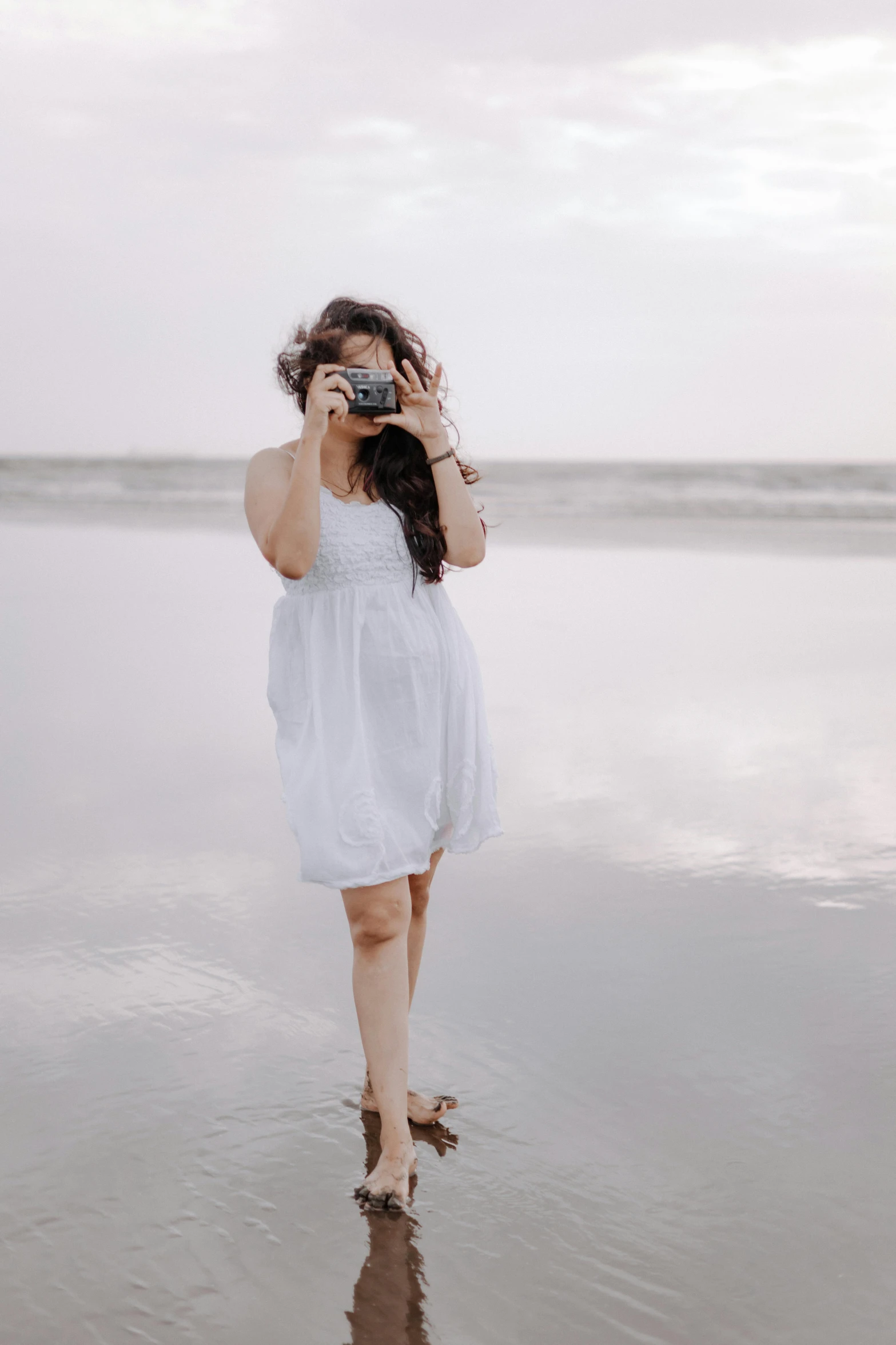 a woman walking on the beach in front of a body of water holding a camera