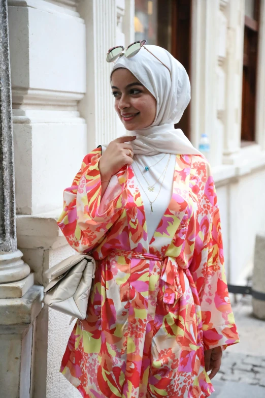 a girl with sunglasses smiling, wearing a colorful shirt and a white hijab