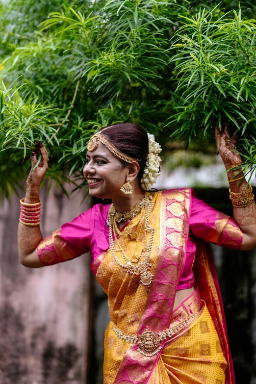 a woman in an orange and yellow colored sari carrying bamboo nches on her shoulders