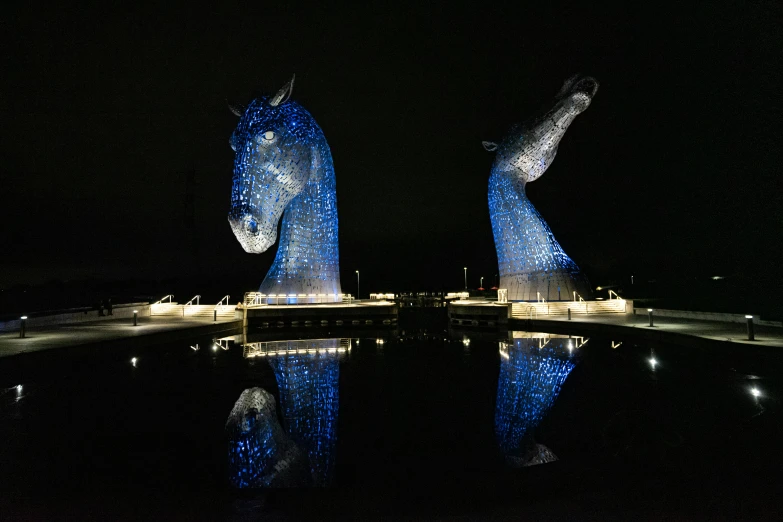 a large blue horse statue at night reflecting in water