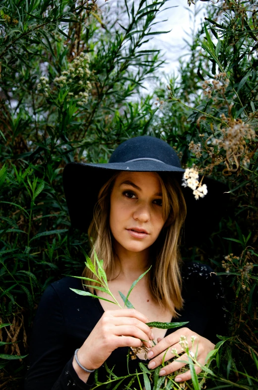 a woman in a hat is standing among plants